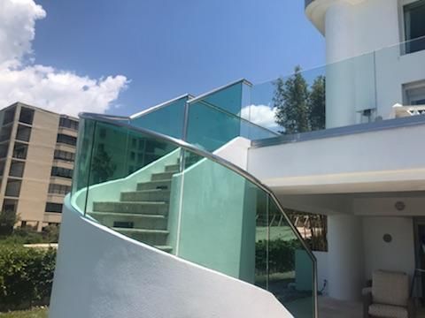 Spiral staircase with turquoise glass panels, stainless steel handrails, and a white stucco wall, against a blue sky.