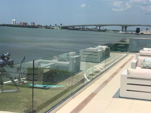 Rooftop patio overlooking water and bridge, with white furniture, clear railing, and sculptures.