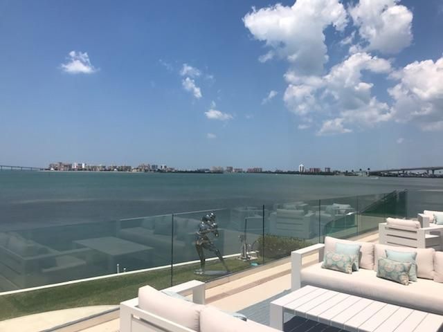 Outdoor seating area overlooking a calm body of water and distant cityscape on a sunny day.