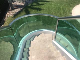 Stone steps descend from a curved, glass-railed patio, with greenery in the background.