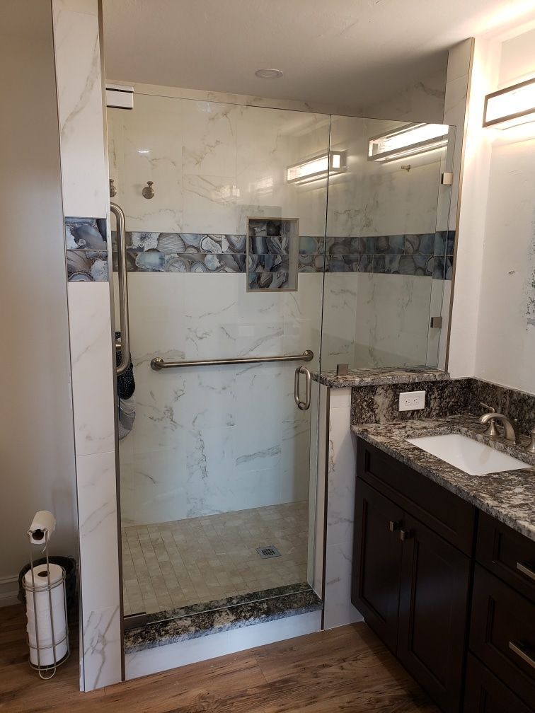 Modern shower with glass doors and marble walls, next to a dark wood vanity.