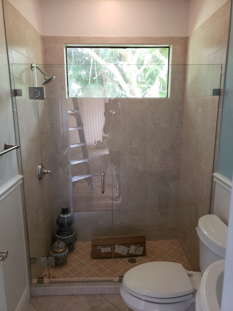 Small bathroom with glass shower, toilet, and window. Tan tile, beige and blue walls, natural light.