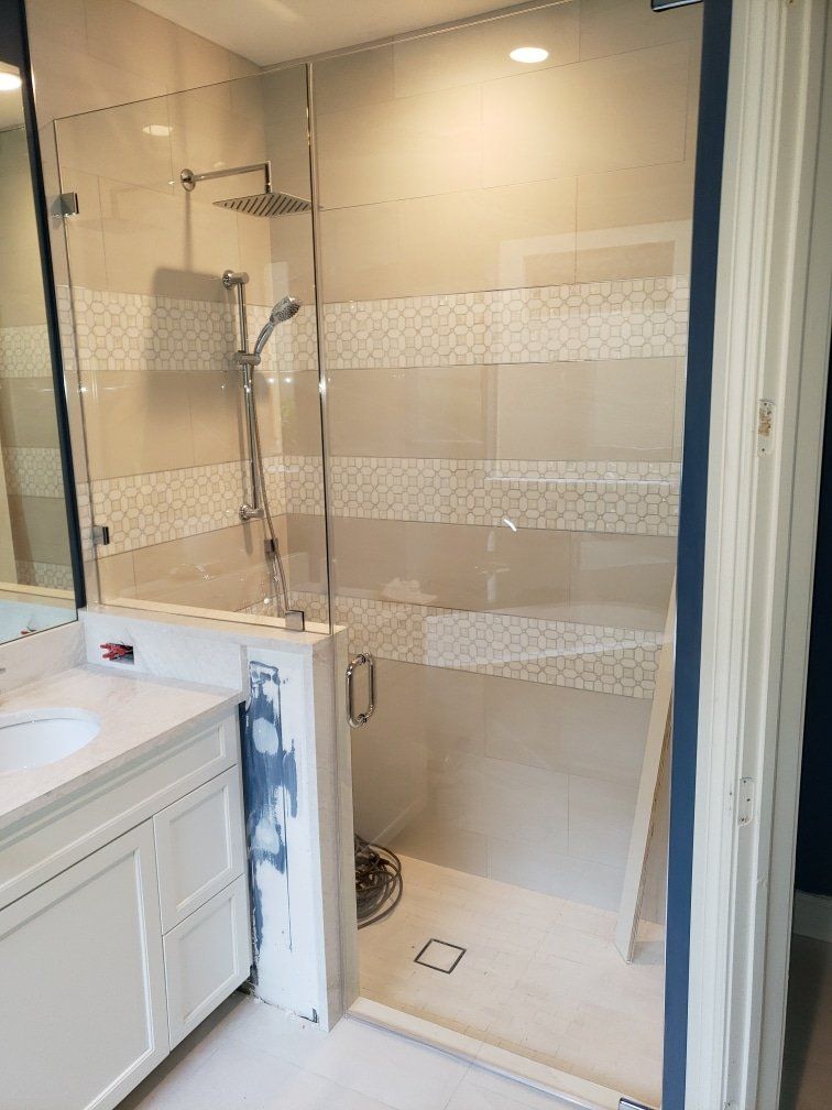 Modern bathroom with glass shower, white vanity, beige tile, chrome fixtures.