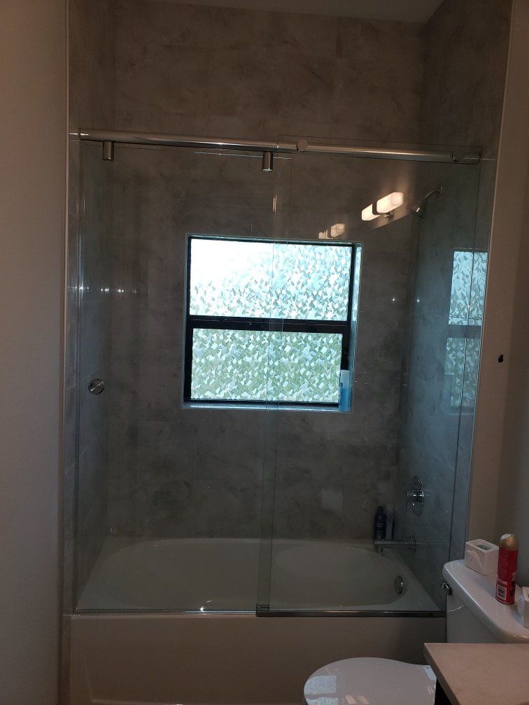 Bathroom with a bathtub, glass shower doors, a window, and toilet.