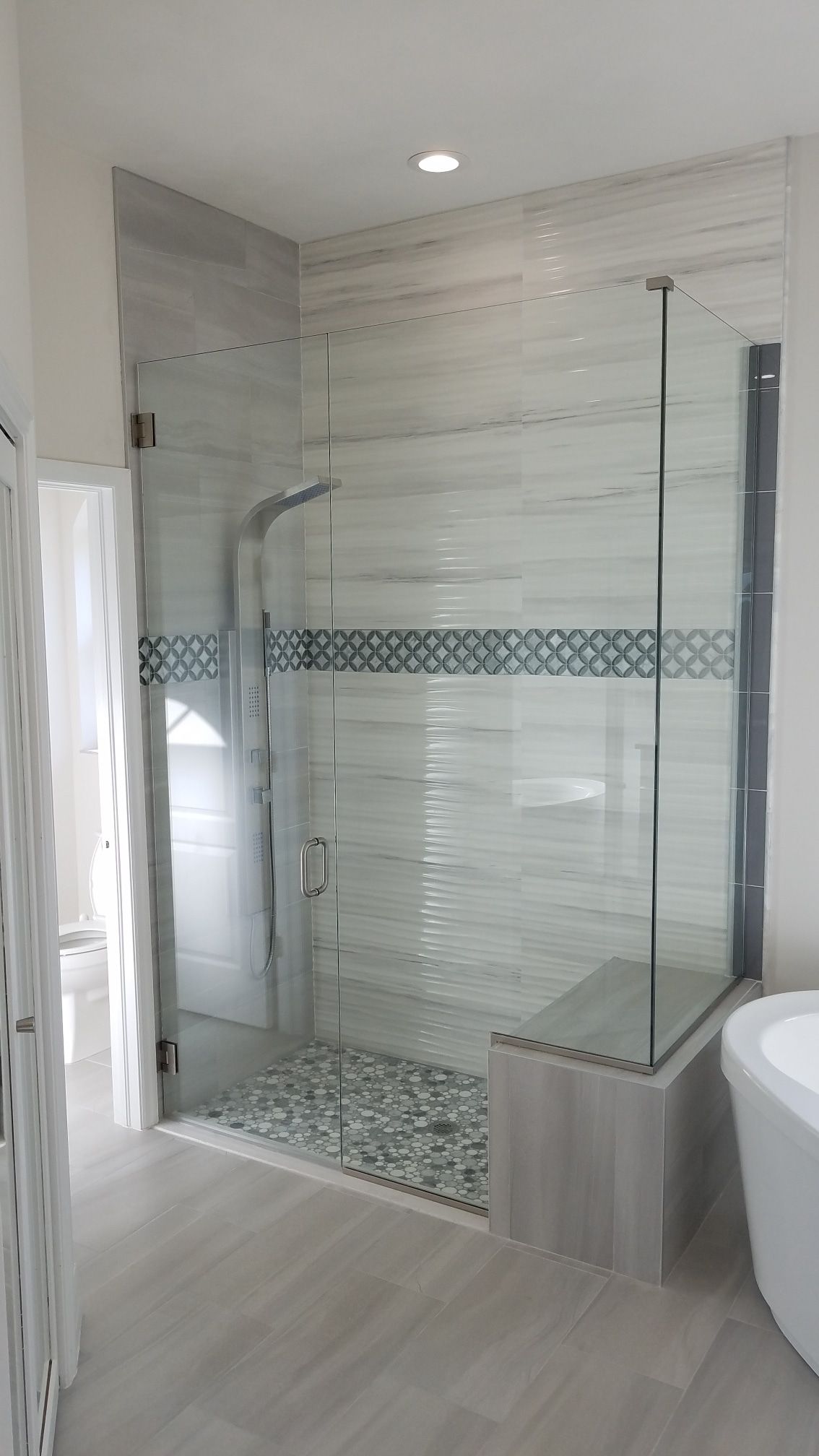 Glass shower with gray and blue tile accents, pebble floor, and a built-in bench.