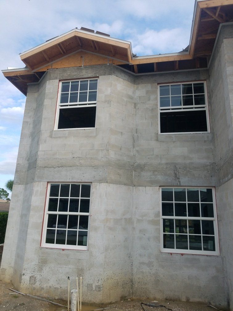 Exterior of a two-story concrete block house under construction with installed windows.