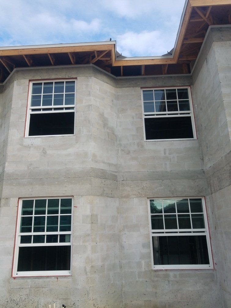 Gray concrete building exterior with four white-framed windows under construction, blue sky.
