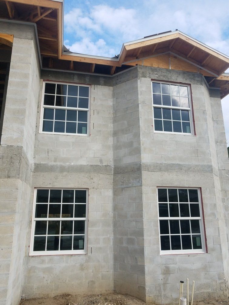 Two-story building under construction with four white-framed windows, gray concrete block walls, and exposed wooden roof framing.