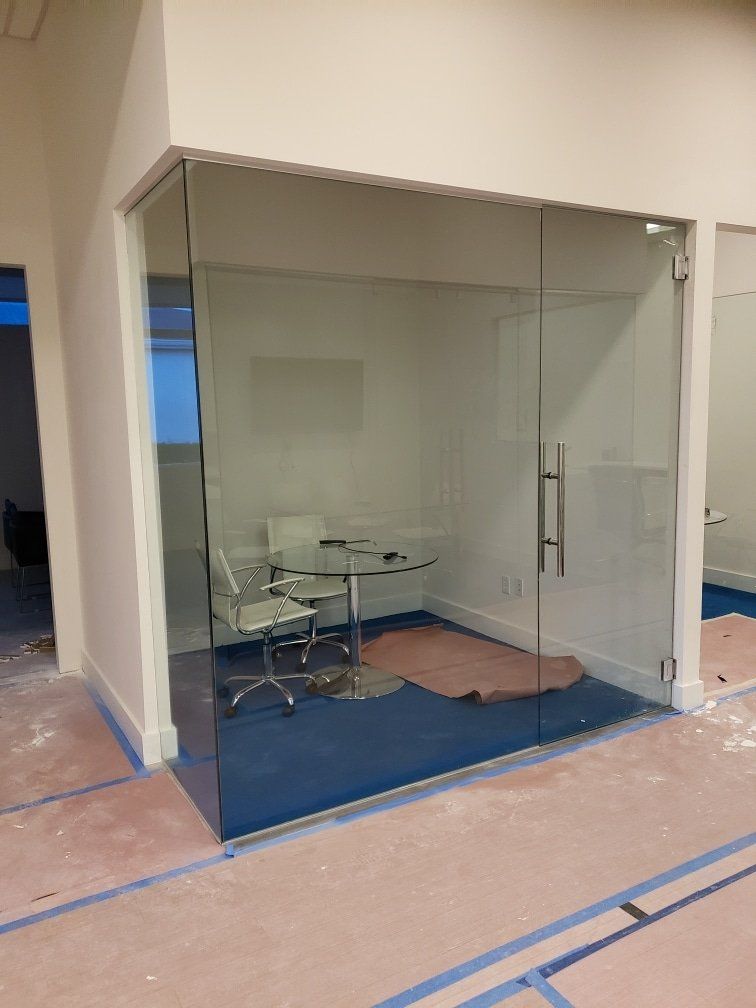 Glass-walled office space with a table and chairs; white walls and blue flooring are visible.