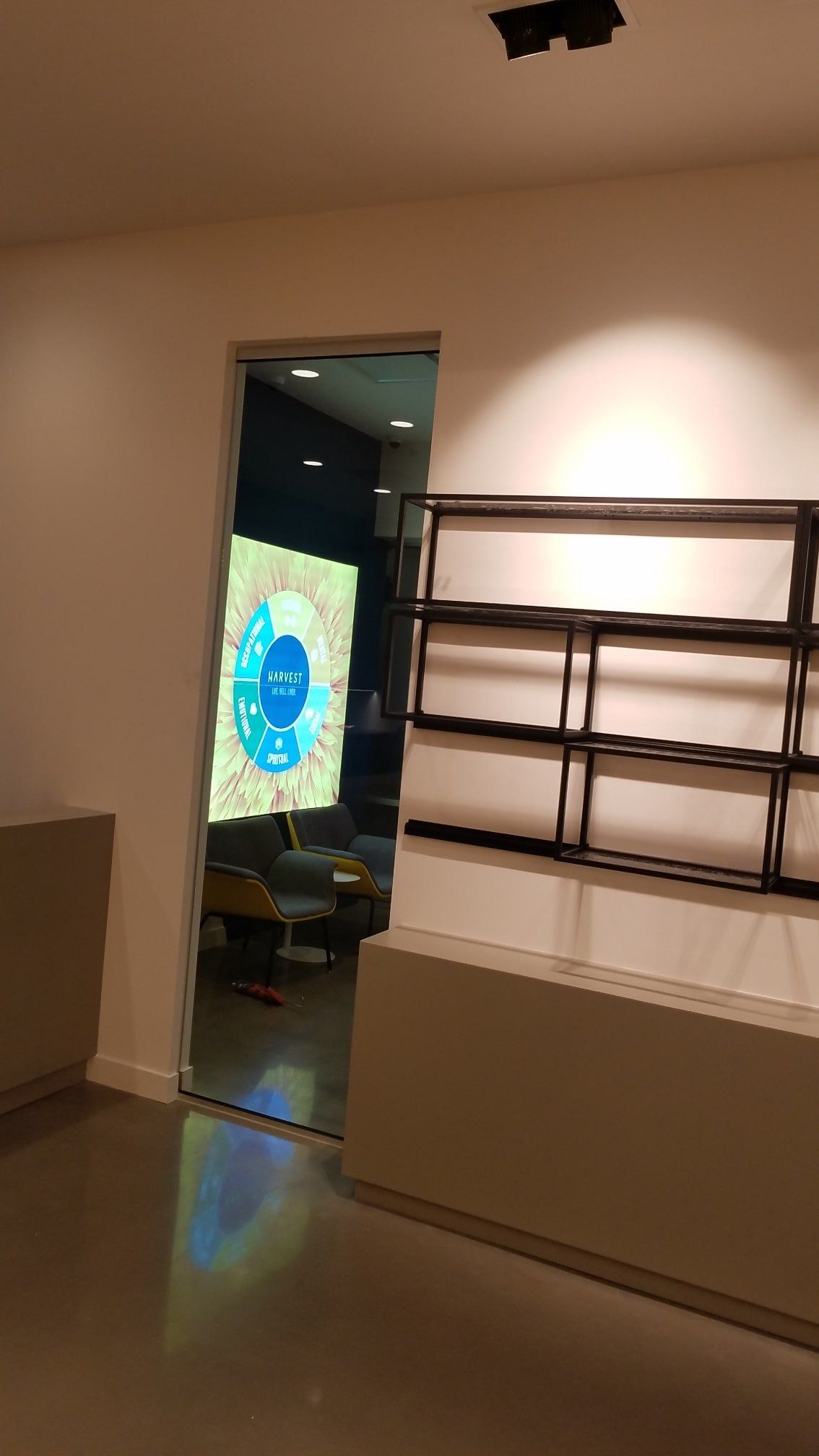 A retail store interior with a doorframe leading to a room with a digital display. A black shelving unit is on the right.