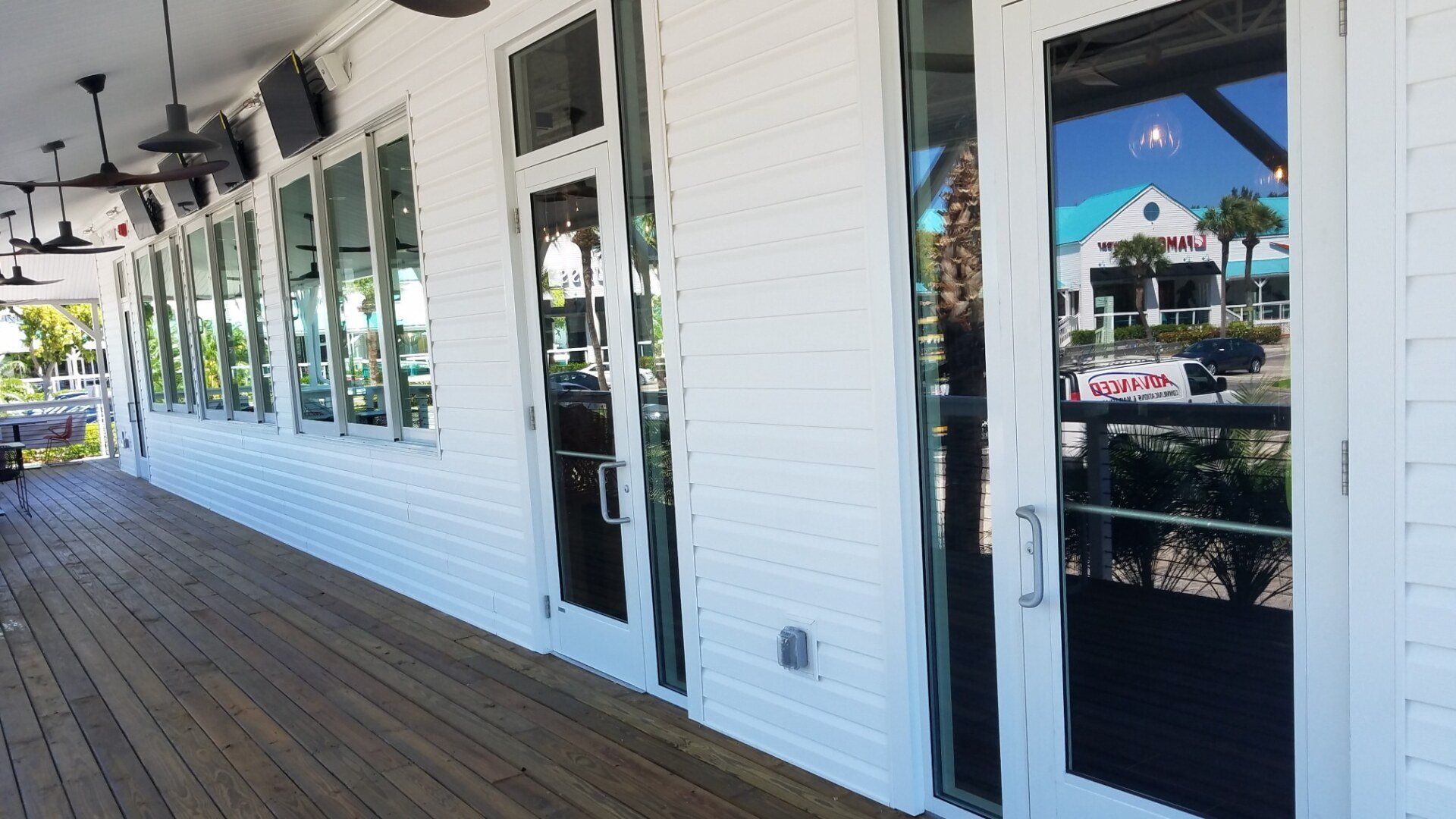 Exterior view of a white building with a wooden deck. Large glass doors and windows reflect the surroundings.