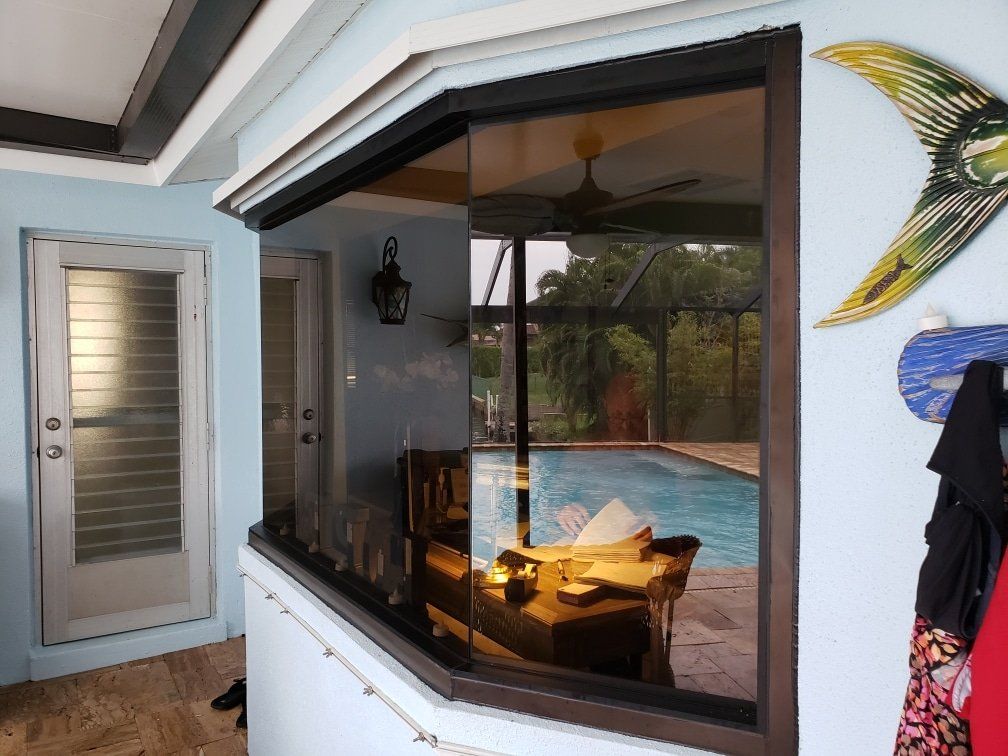 A partially open glass window shows a pool, furniture, and sky. Building has a door, a wall and ceiling.
