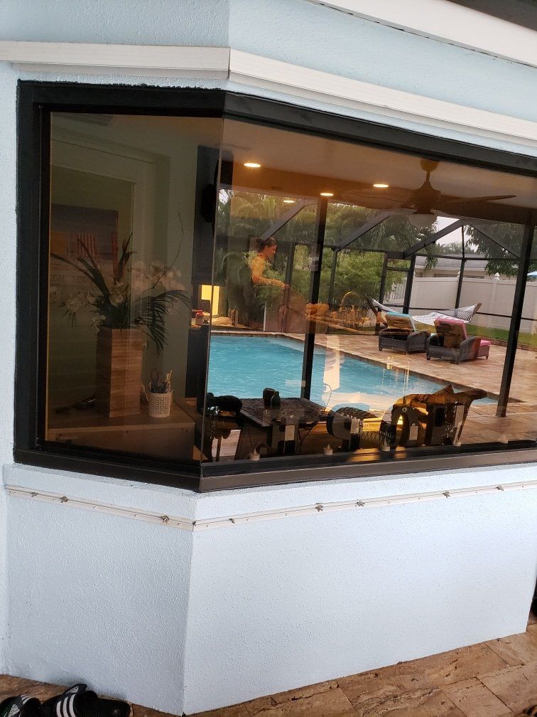 Corner window of a house overlooking a pool and patio. Black frames, white walls, and reflective glass.