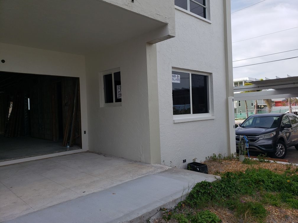 Exterior view of a two-story white building with a garage, car parked beside it, concrete pathway.