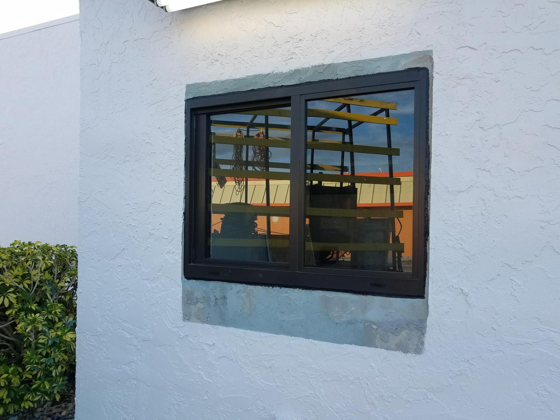Window with dark frame on a stucco wall, reflecting a yellow and orange structure.