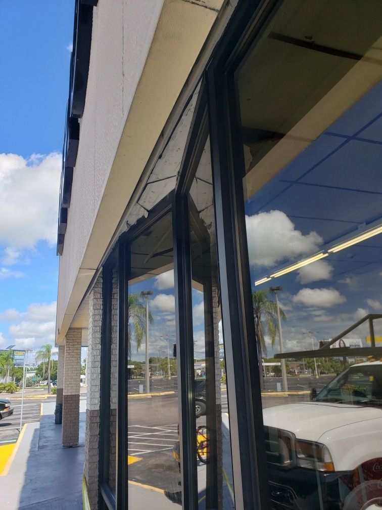 Exterior of a commercial building with large glass windows, reflecting sky and vehicles.
