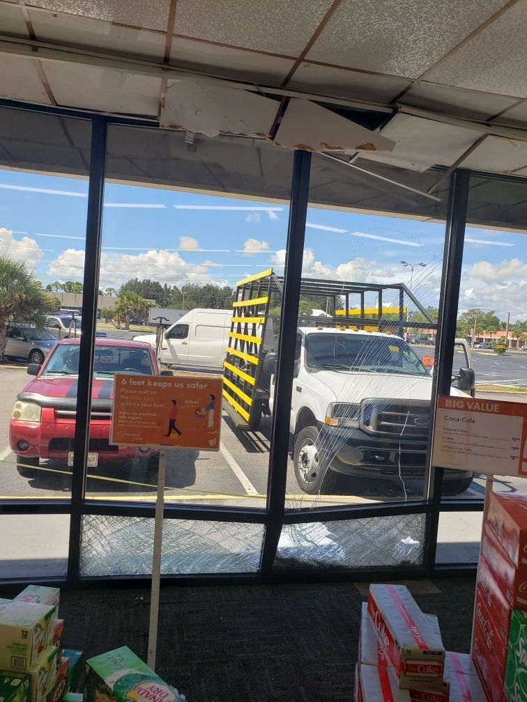 View through a window of a store with parked vehicles. Red car, white van, and truck with yellow sides are visible.