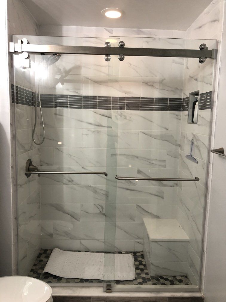 Modern shower with sliding glass doors, marble-look tiles, and a built-in bench, with a towel on the floor.