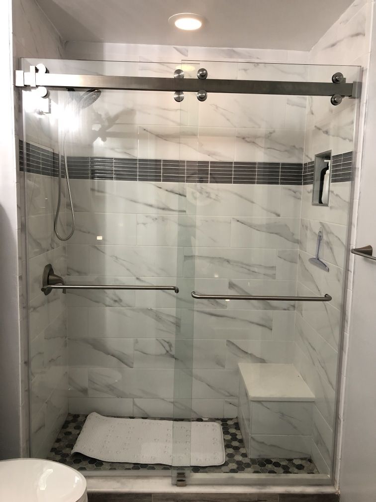 A modern bathroom shower with marble-like tiles and a sliding glass door. Includes a seat and towel rack.