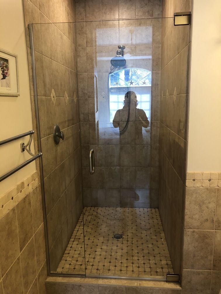 Shower with glass door, beige tile, and a person reflected in the glass.