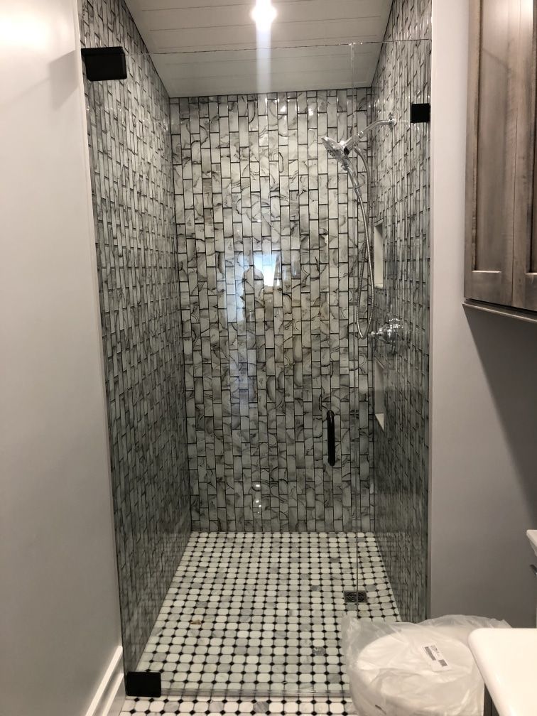 Narrow shower stall with mosaic tile walls, black & white floor tile, glass doors.