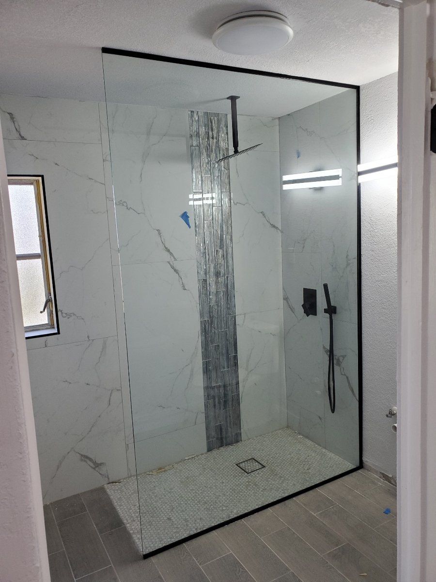 Modern shower with black trim, marble-like tile, and a rainfall showerhead; a finished bathroom interior.