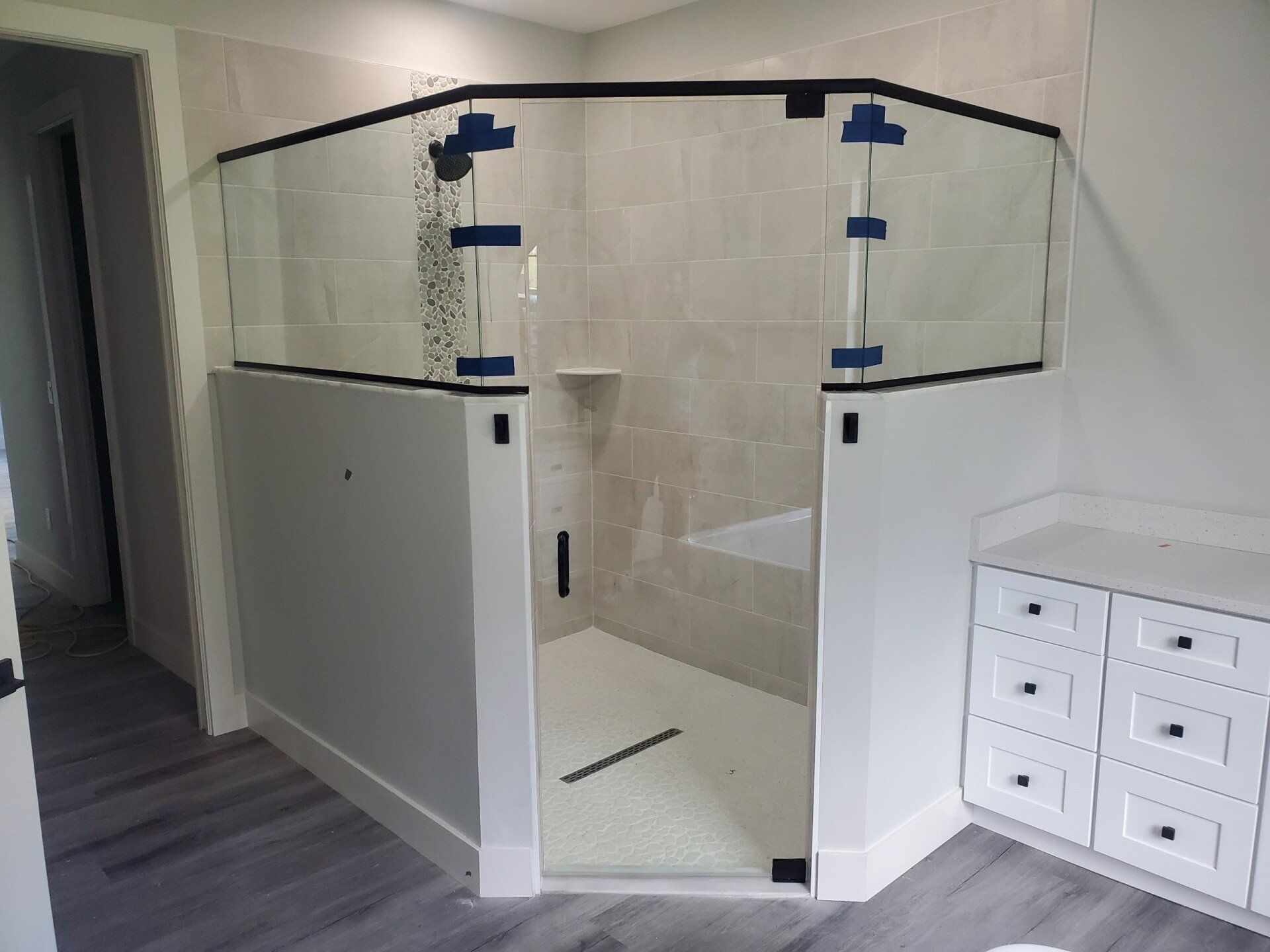 A modern, accessible shower with glass doors, white walls, and gray tiled floor.