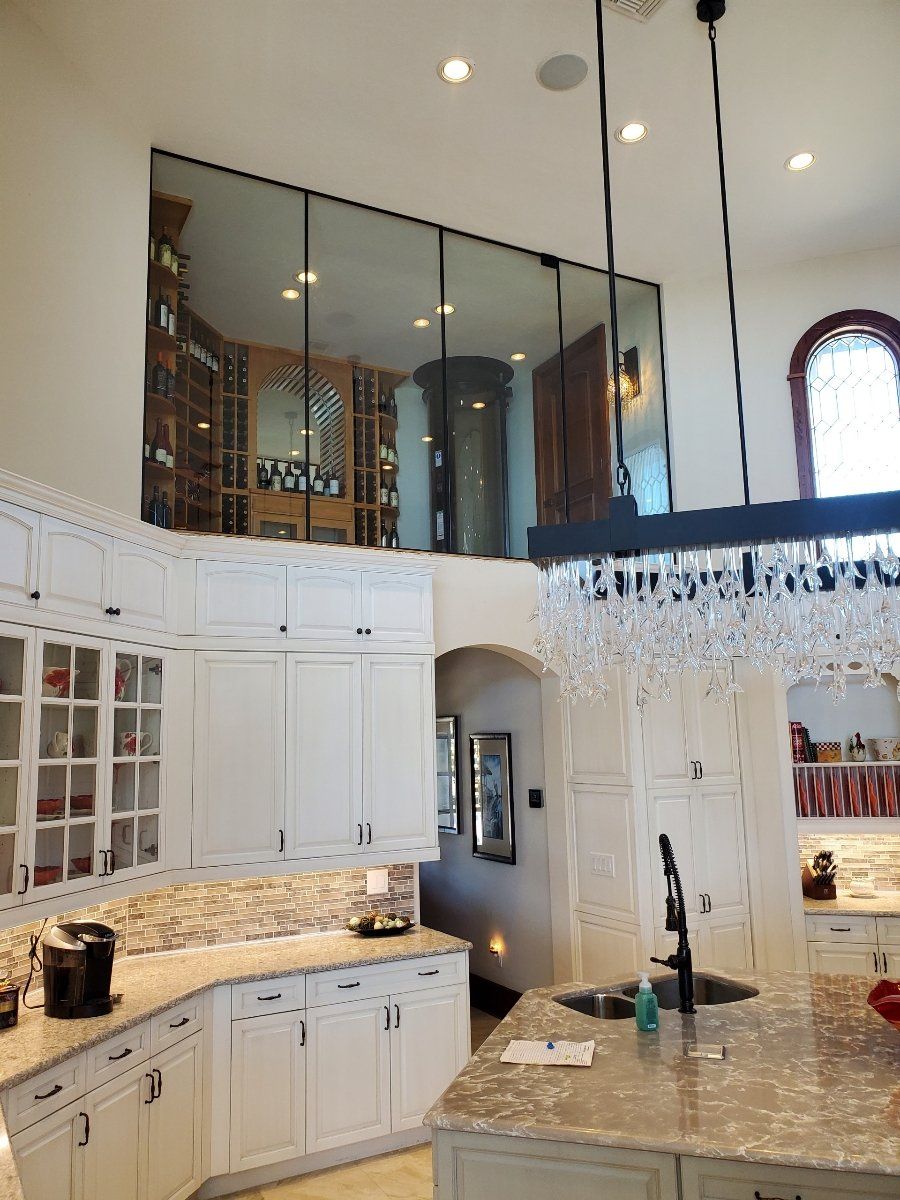 Kitchen with a large mirror reflecting a wine cellar. White cabinets, granite countertops.
