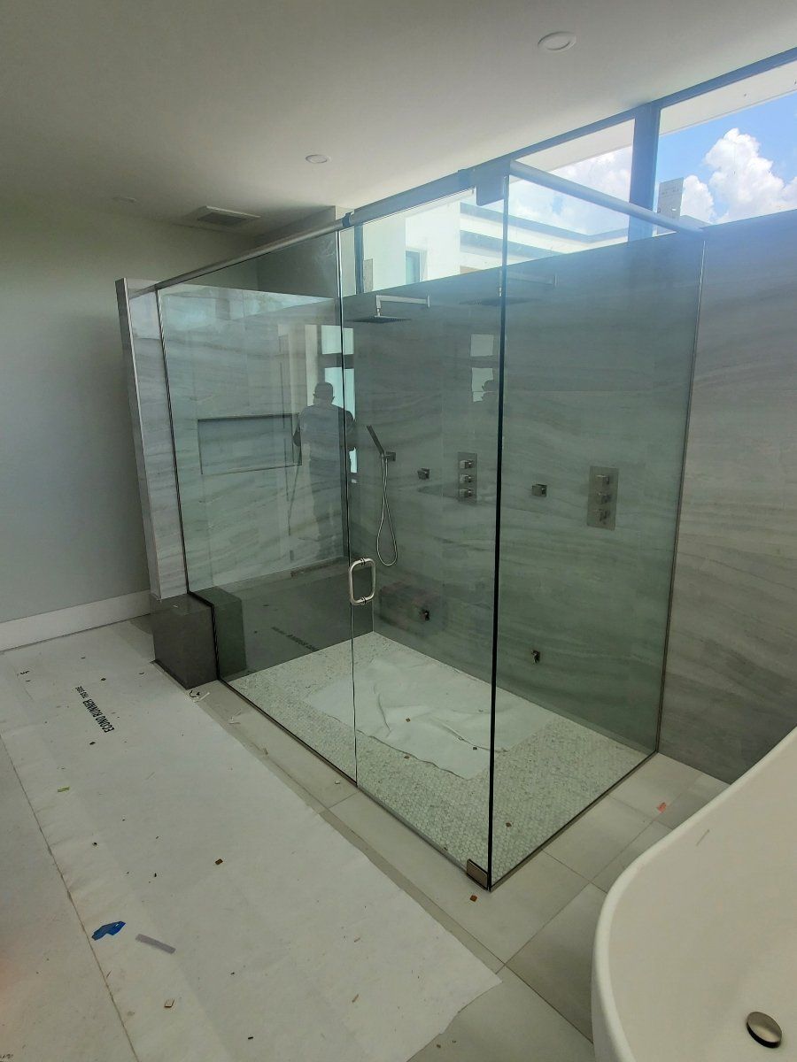 Modern glass shower with gray stone wall and white floor.