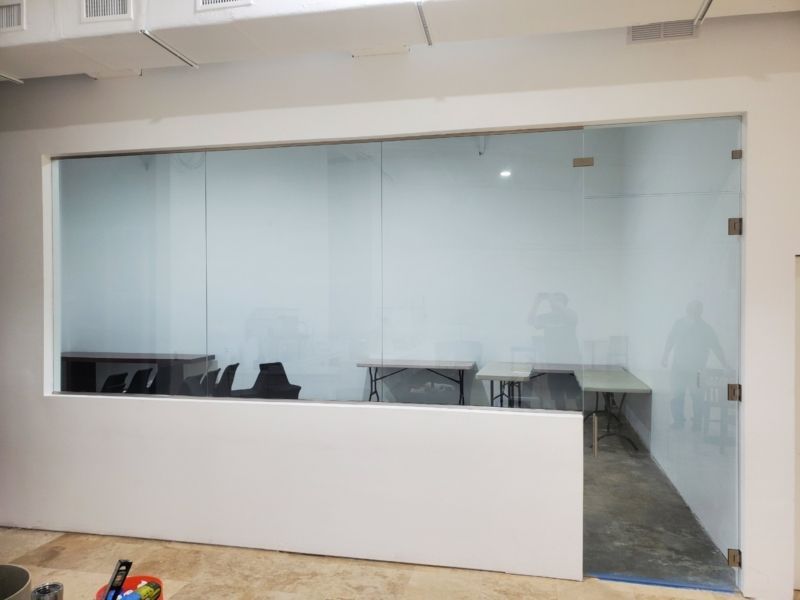 Glass-walled office space with tables and chairs inside, white walls and a low white wall in front.
