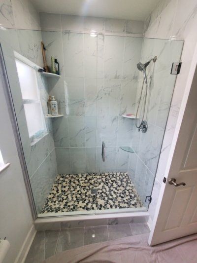 Shower stall with pebble floor, white marble tile, glass door, and shelves.