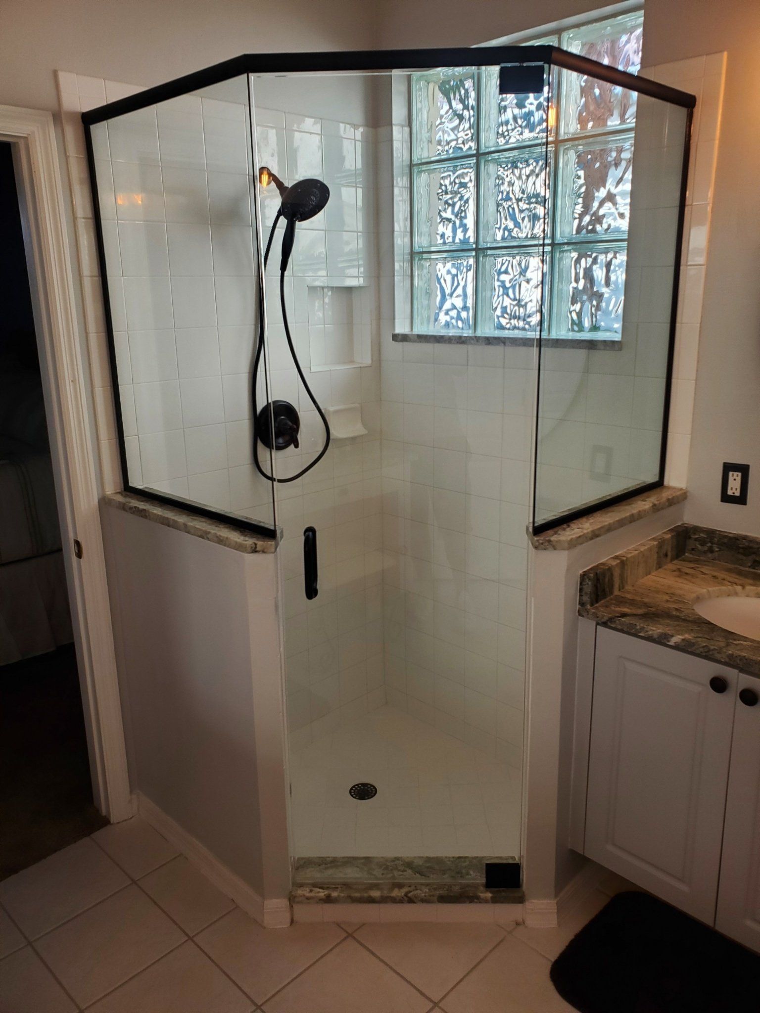 A modern shower stall with black trim, a glass door, and a black shower head in a bathroom.