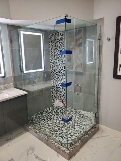 A corner shower with glass walls and a mosaic floor. Features a gray and white color scheme.