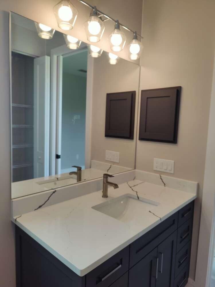 Bathroom vanity with white countertop, dark cabinets, and large mirror.