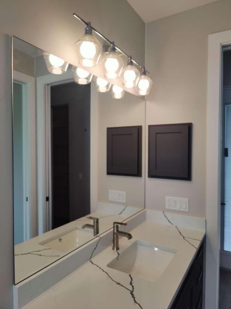 Bathroom with mirror, vanity, and modern light fixture; neutral walls.