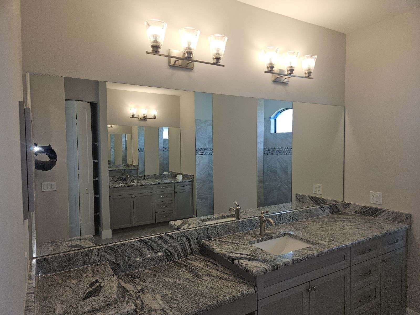 Bathroom with granite countertop, gray cabinets, large mirror, and two light fixtures.