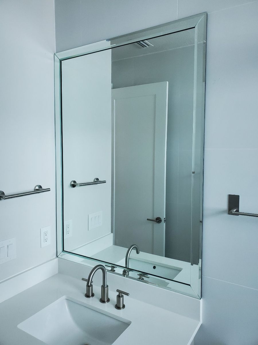 Bathroom with a large mirror above a sink. White walls, countertop, and door. Silver fixtures.