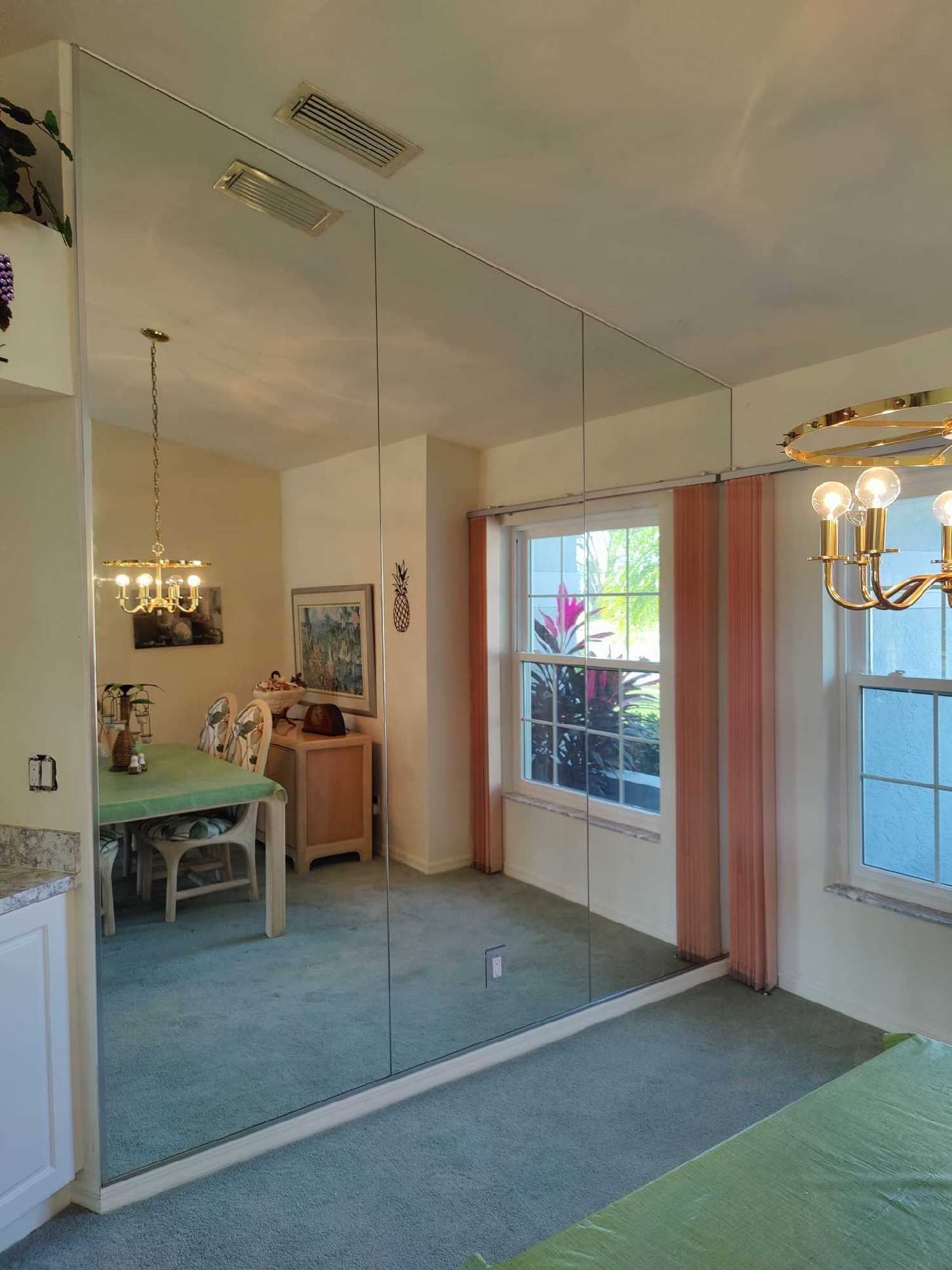 Dining room with mirrored wall, two chandeliers, a table with a green tablecloth, and a window.