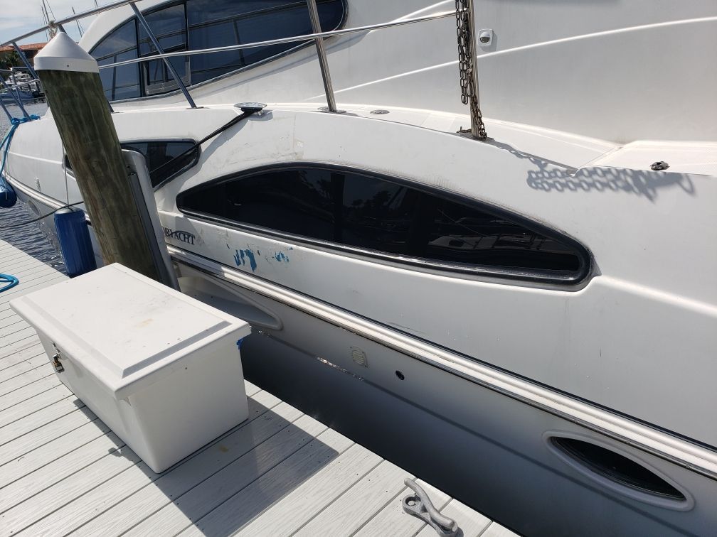 White boat docked at a marina, with a white box, blue post, and dark tinted window.