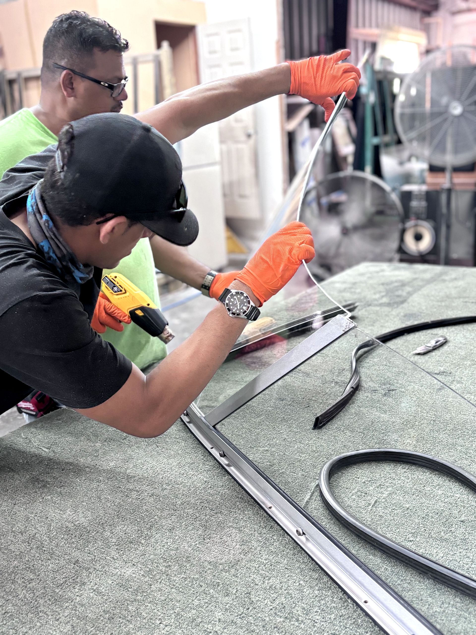Two people wearing gloves working on a window frame, one with a heat gun.