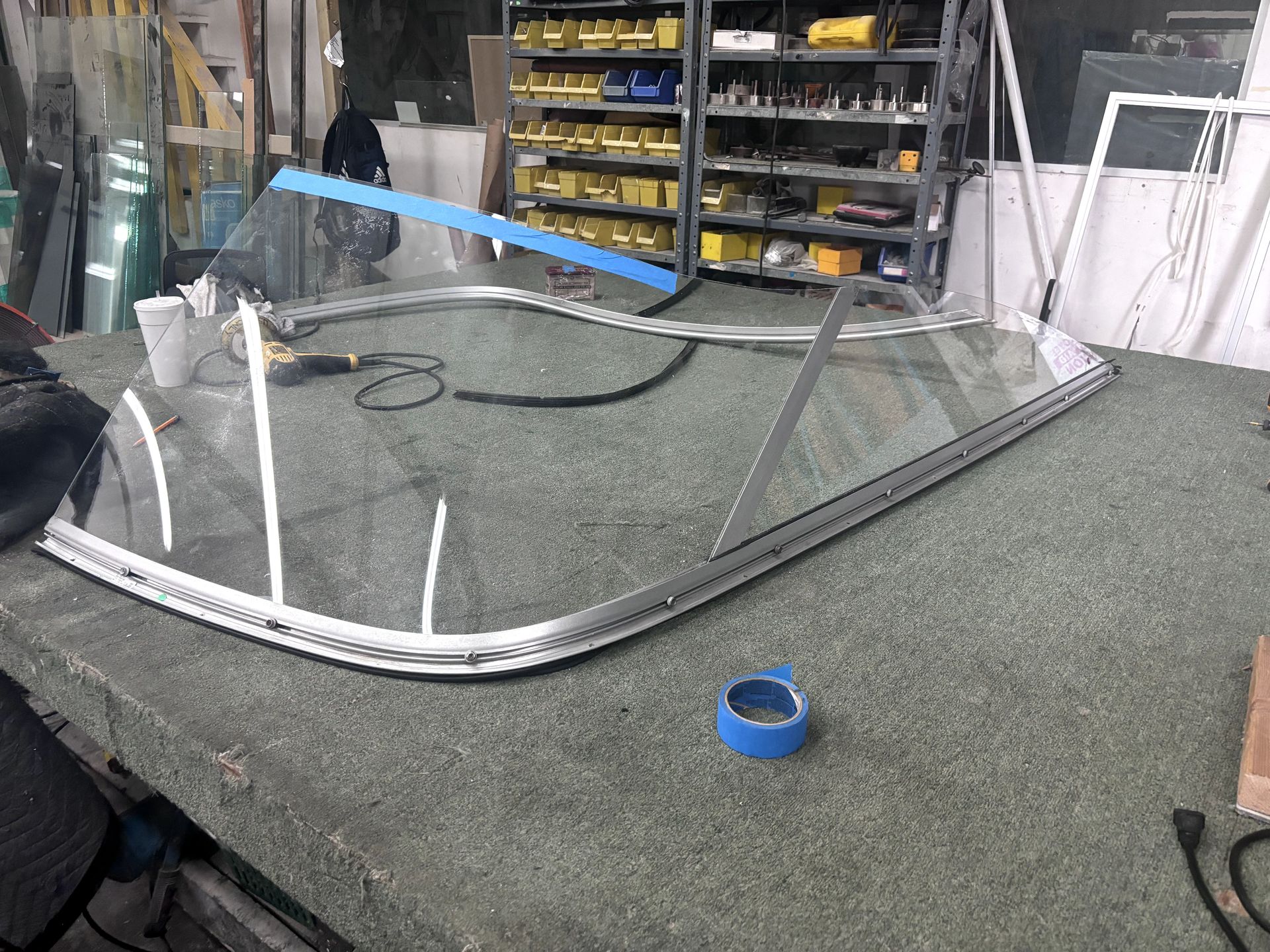 A large pane of curved glass with metal framing on a workbench in a workshop setting.