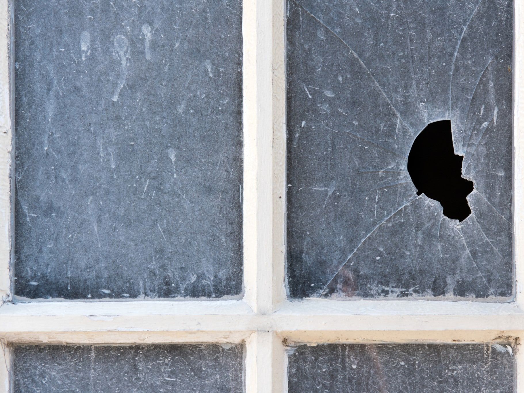 Broken window pane with hole. White frame. Grimy, streaked glass.