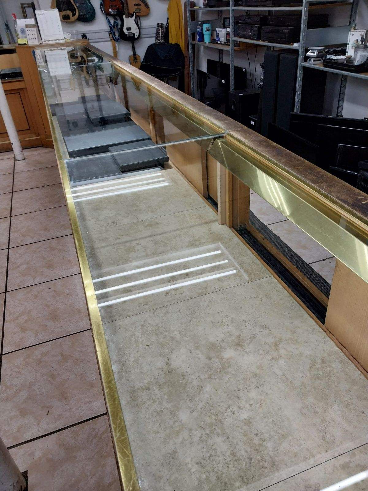 Long, empty display case with gold trim and glass top, in a store setting.