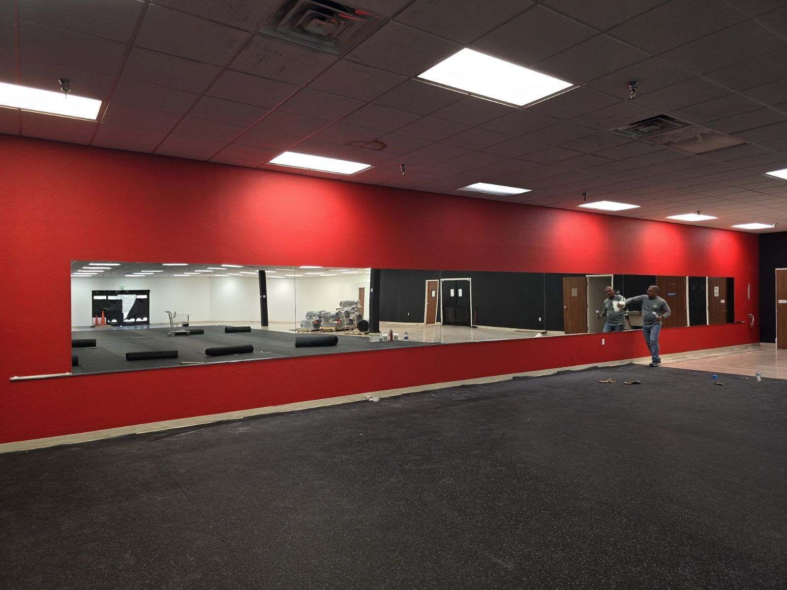 A large red-walled room with a wall mirror, black rubber flooring, and a person standing near the door.