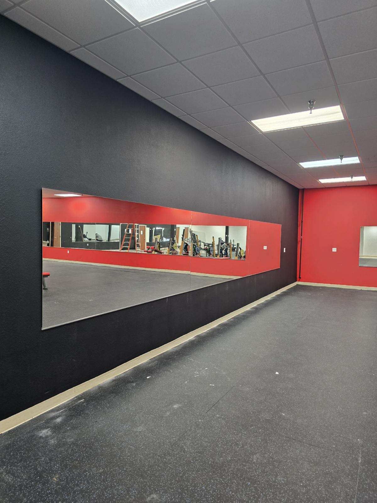 Gym interior: black wall with long mirror, red walls, black floor, and exercise equipment reflections.