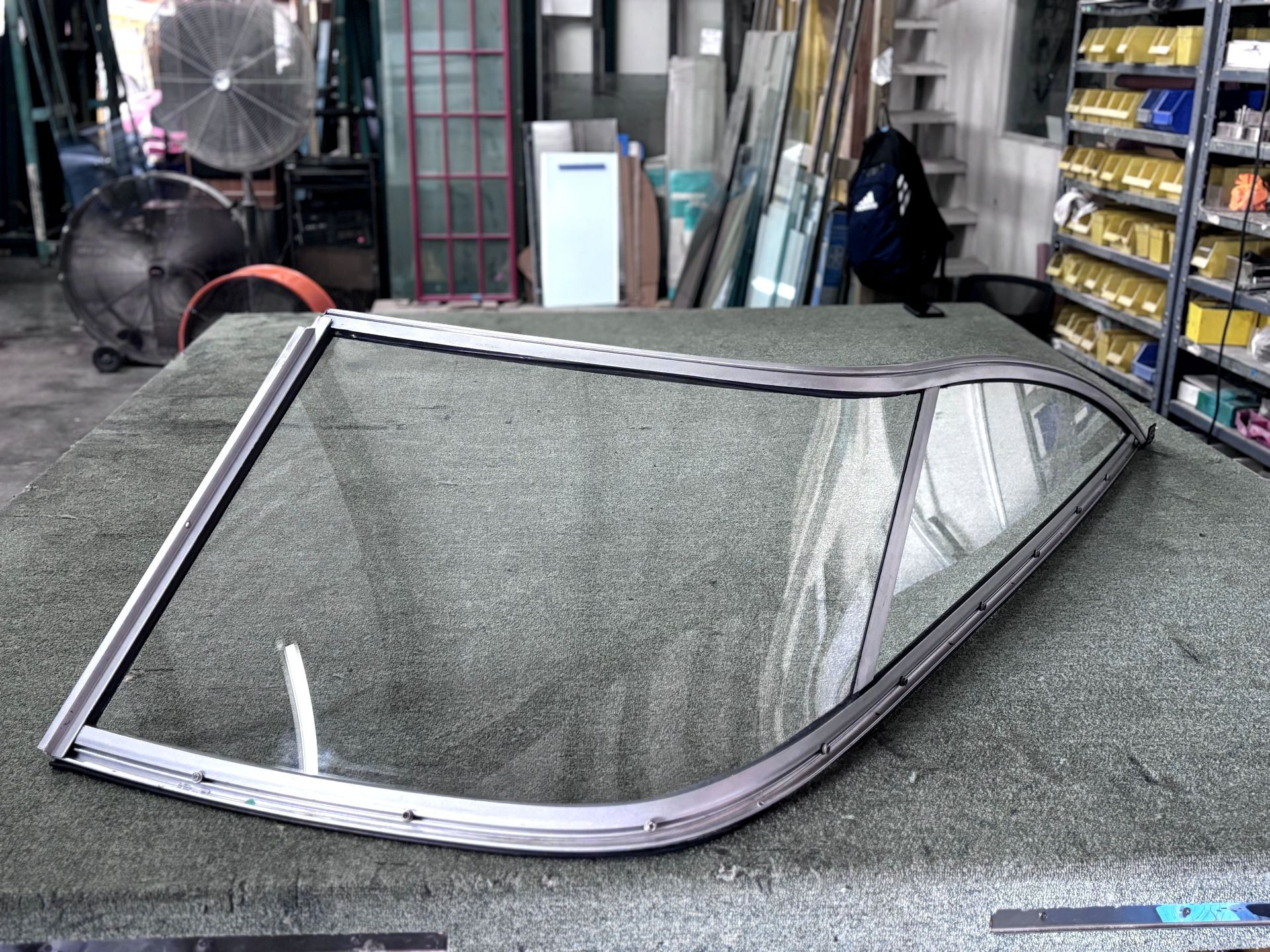 Curved window frame with glass laid on a green surface in a workshop setting.