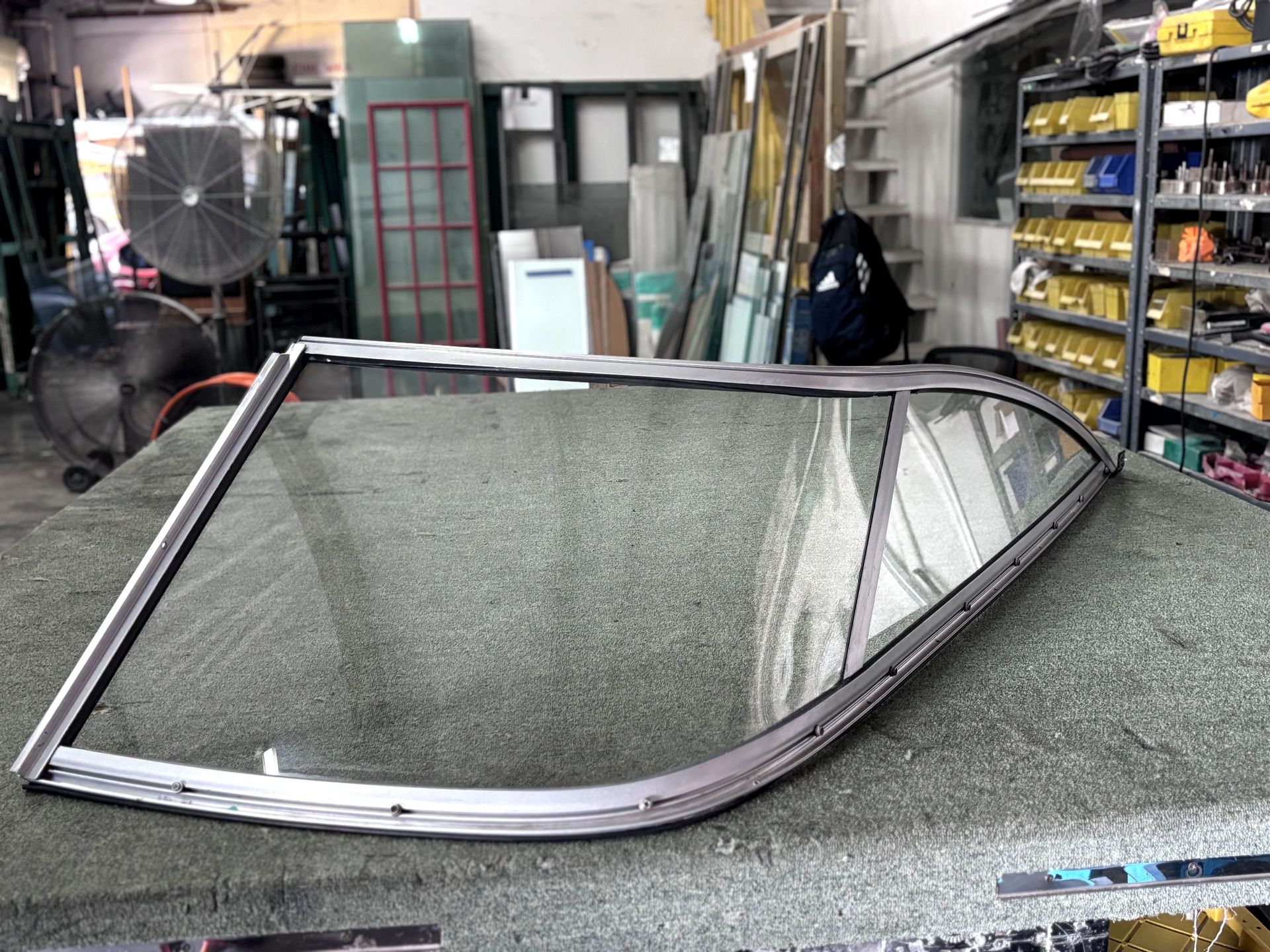 A large, curved window frame with glass, displayed on a work table in a workshop setting.