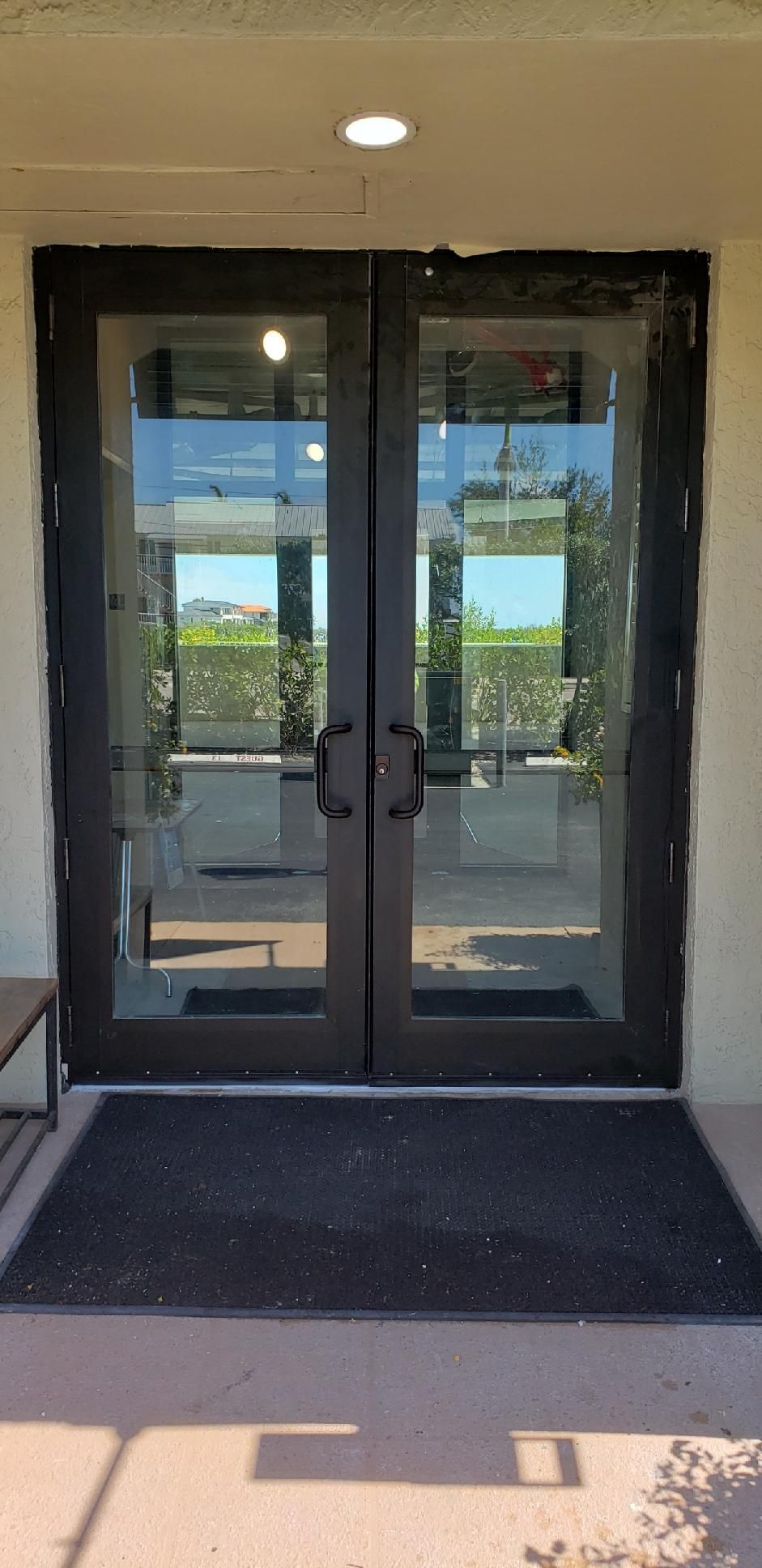Glass double doors with black frames and handles, leading to an outdoor area. A welcome mat rests at the entrance.