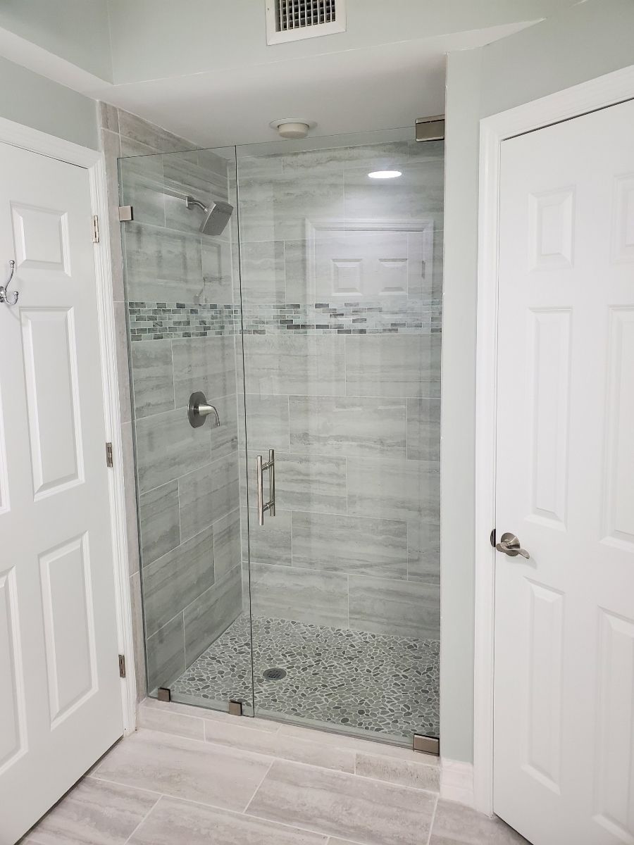 Glass-enclosed shower with gray tiled walls, pebble floor, and two white doors on either side.
