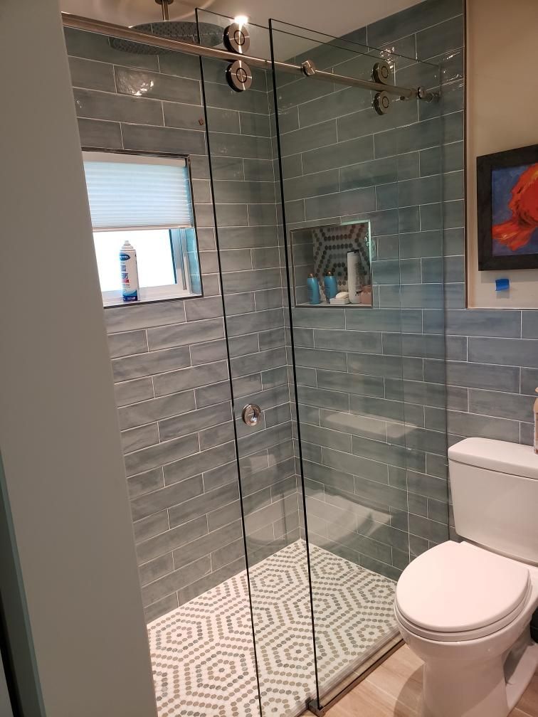 Modern bathroom with teal tiled shower, glass door, and white toilet.